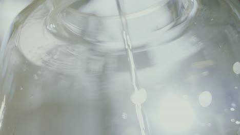 close up shot of distilled alcohol flowing inside a glass jar, industrial process in a gin distillery production