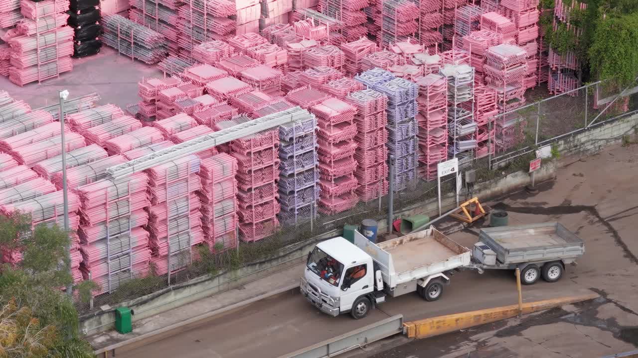 Drone footage captures trucks and workers in a Gold Coast junkyard. Bright lighting highlights organized stacks of materials