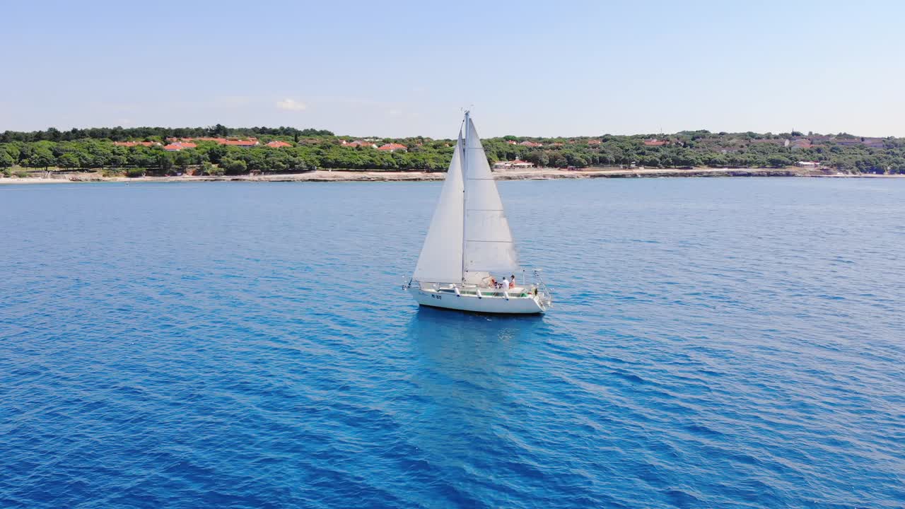 un solitario velero blanco navega a lo largo de la costa verde bajo cielos despejados en tranquilas aguas azules claras
