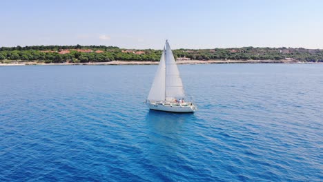 un solitario velero blanco navega a lo largo de la costa verde bajo cielos despejados en tranquilas aguas azules claras