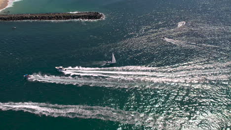 aerial view of drone tracking a yacht sailing out to sea through the sea way avoiding other boats on a beautiful day at the spit gold coast qld australia