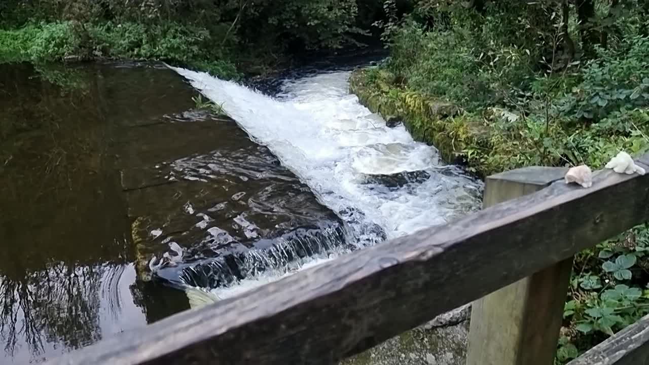 Slow motion rising above wooden fence barrier overlooking fresh cascading stream flowing down rocky stonework