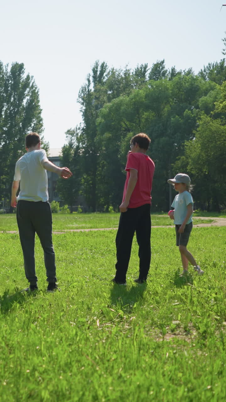 un abuelo lleva a sus dos nietos a estirar los brazos en un campo cubierto de hierba, mientras dos niños más pequeños están de pie con una pelota de fútbol en el fondo