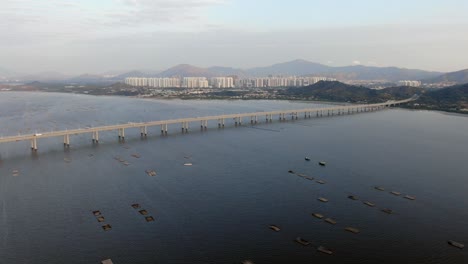 hong kong shenzhen bay bridge with tin shui wai buildings in the horizon and fish and oyster cultivation pools, aerial view