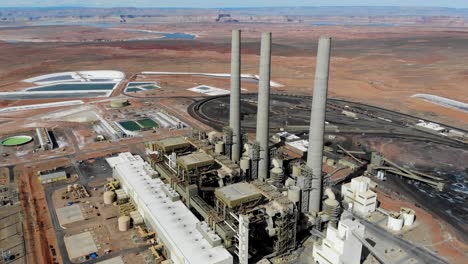 a drone shot of the “navajo generating station”, a massive coal-fired power plant and industrial complex with tall stacks, in the middle of the desert of the navajo nation, located near page, arizona