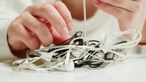 Young woman trying to untangle the headphones close-up. Tangled wires on table. Trying to untangle many messy cables