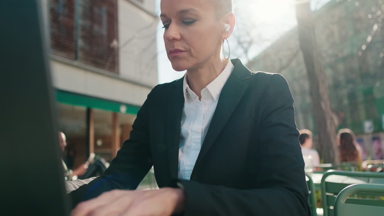 Imprenditrice concentrata che lavora al portatile in un bar all'aperto con la luce del sole