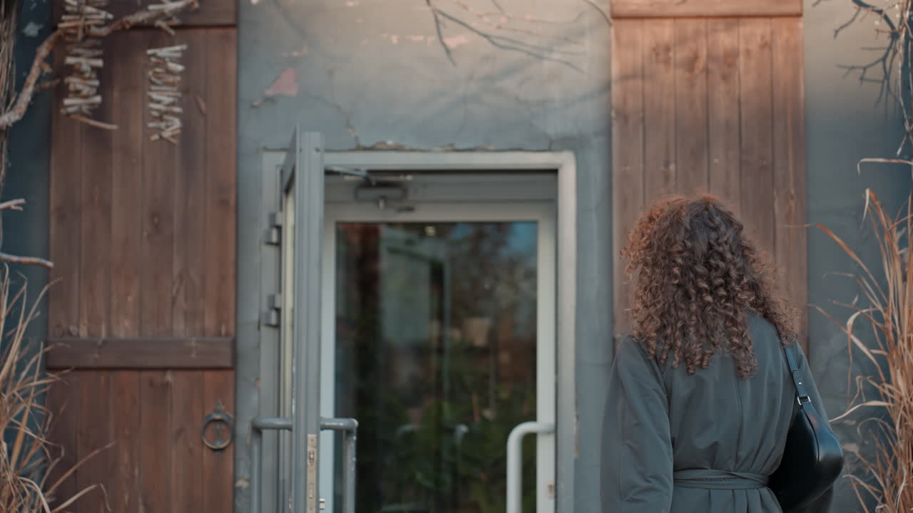 Closeup florist portrait by iron gate, curlyhaired woman smiles near ornate fence, soft daylight, urban storefront background, candid expression, poised before entering rustic shop, natural tones