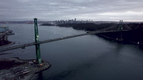 Cars-driving-along-Lions-Gate-Bridge-illuminated-at-dusk-with-cityscape-in-background,-Vancouver-in-Canada