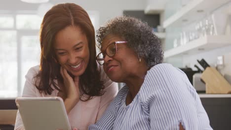 Senior-mixed-race-woman-using-a-digital-tablet-with-her-daughter,-in-social-distancing-