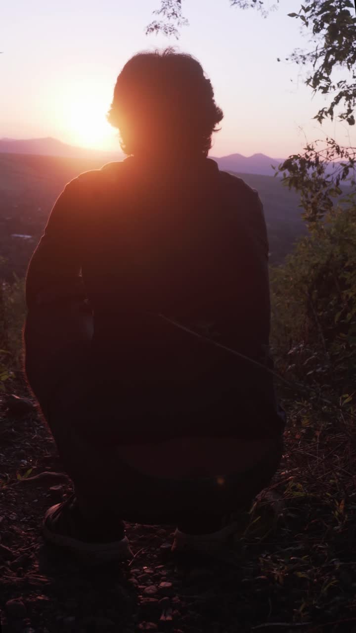 Silhouette di persona accovacciata che guarda il tramonto sulle montagne