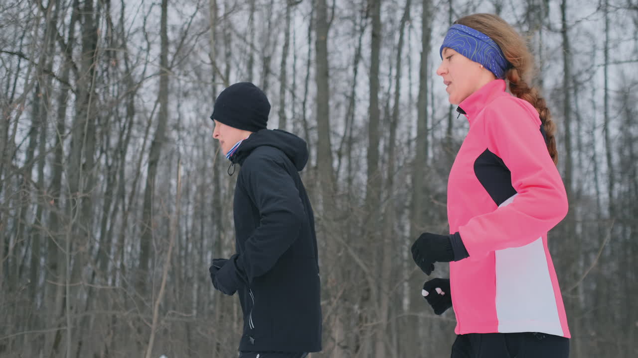 겨울 아침에 숲을 통해 운동복을 입고 달리는 긍정적이고 아름다운 젊고 건강한 커플
