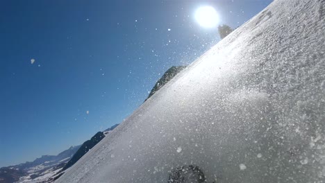 a skier going down a steep slope, in the background a blue sky with bright sun and snow rising from the skis view from the skier’s back