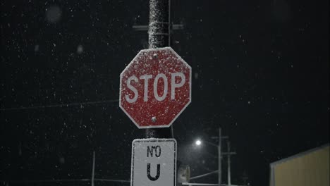 winter snowfall at night snowing on stop sign in city street in street light