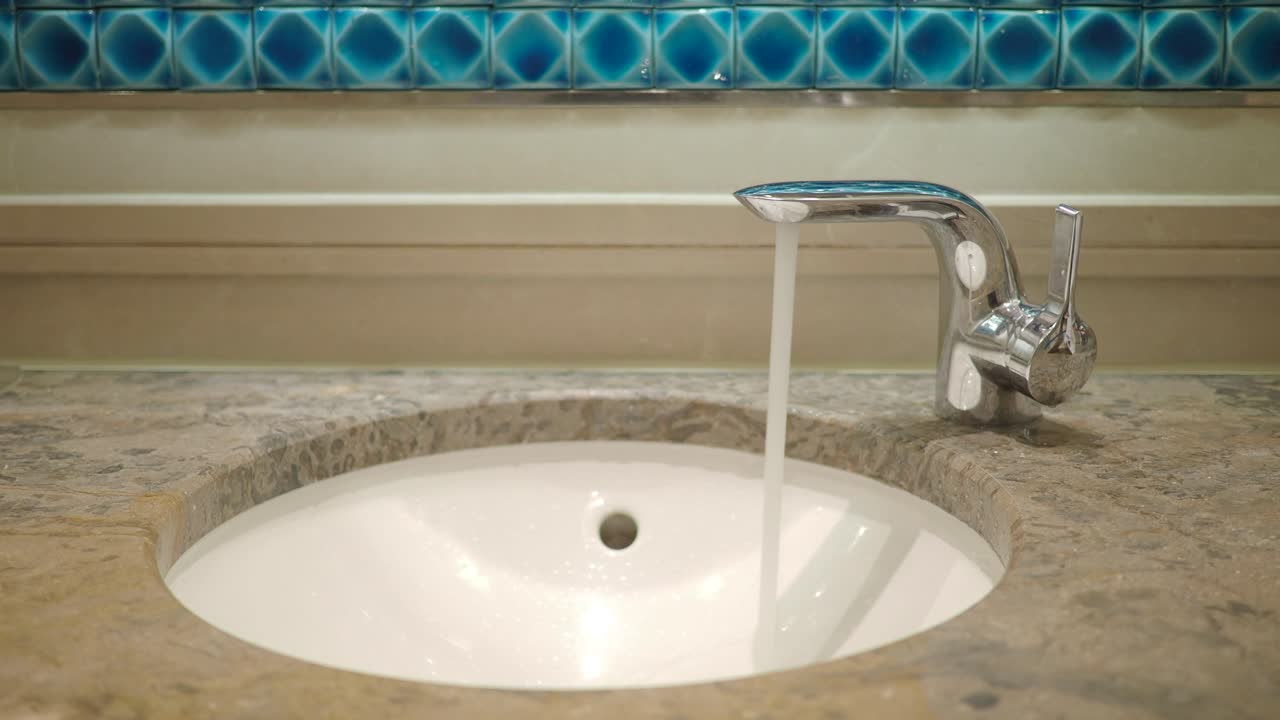 Beyaz banyo lavabosuna krom musluktan akan su