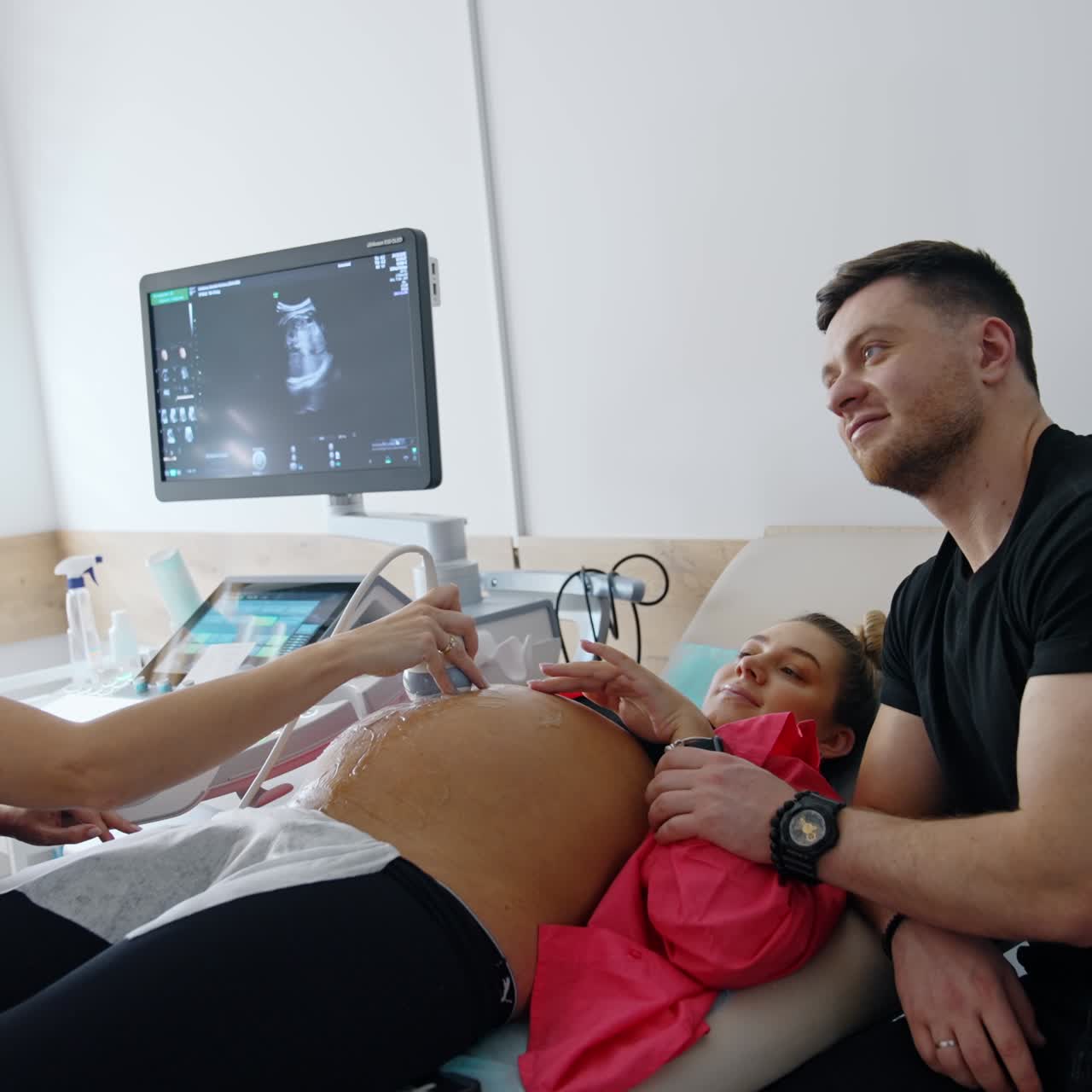 Pregnant lady is examined by doctor on the ultrasonic machine. Loving man caresses his wife's belly