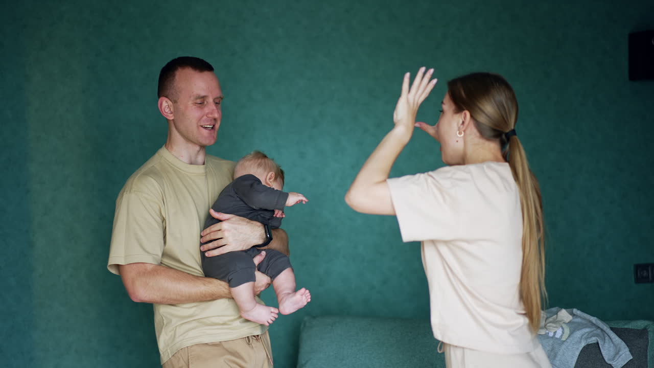 Caucasian man holding a cute little infant in front of him. Mom plays with a baby and kid is happy.