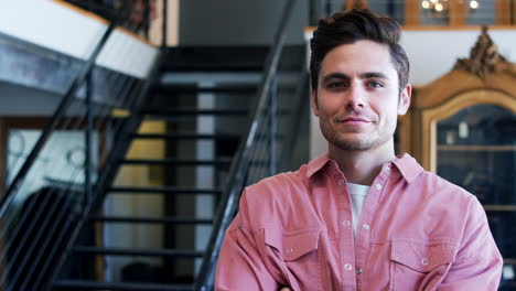 Portrait-Of-Smiling-Male-Owner-Of-Fashion-Store-Standing-In-Front-Of-Clothing-Display