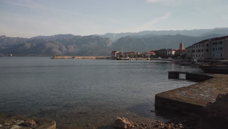 Slow-evening-pan-of-Croatian-village-and-calm-bay,-mountains-behind