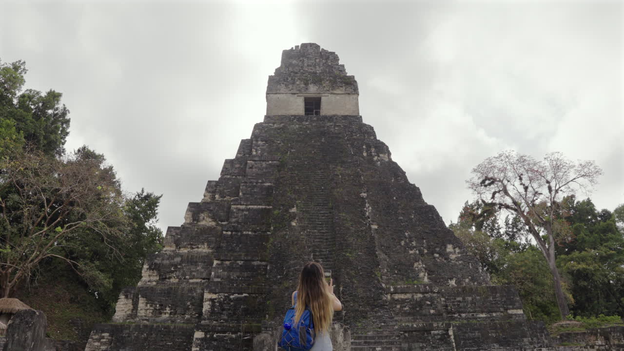 Tourist woman turn to photograph Tikal Pyramid temple I Guatemala. Traveler mobile phone.Slow motion