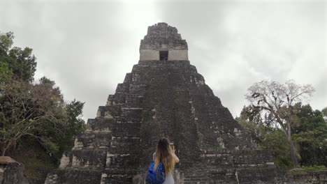 tourist woman turn to photograph tikal pyramid temple i guatemala. traveler mobile phone.slow motion