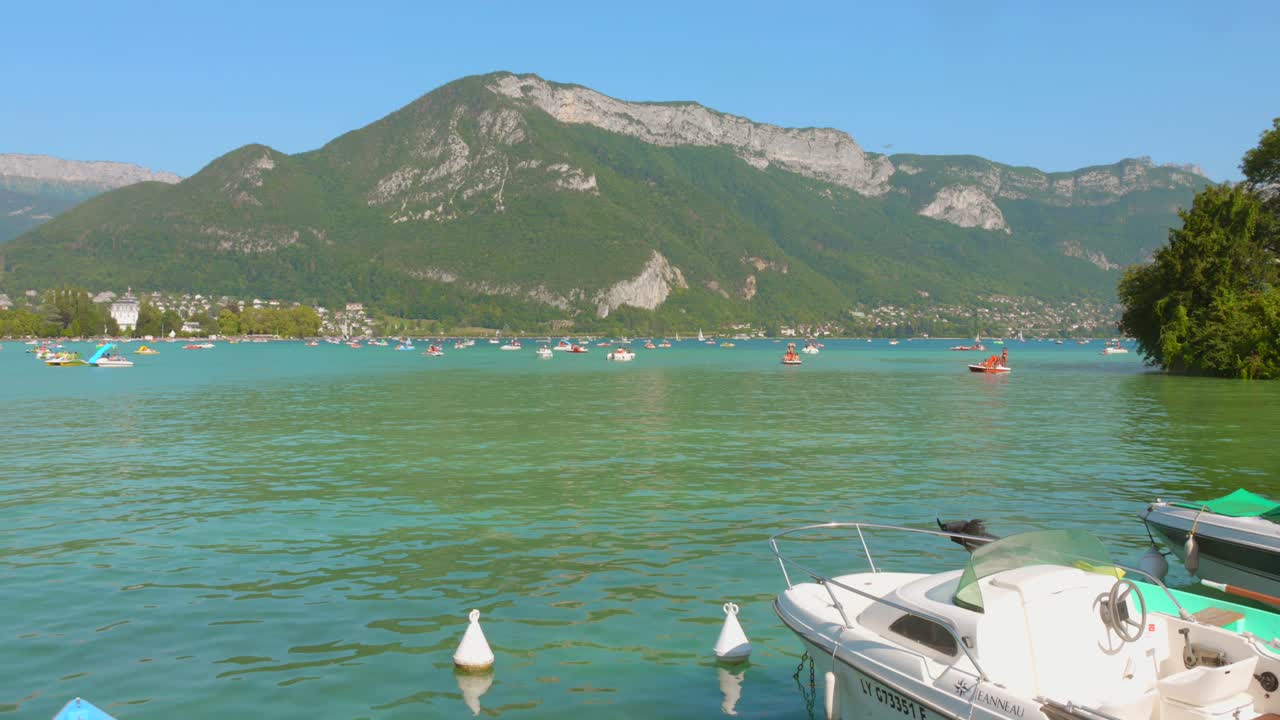 Profile view of tranquil Lake Annecy surrounded by green mountains during daytime in Annecy, France.
