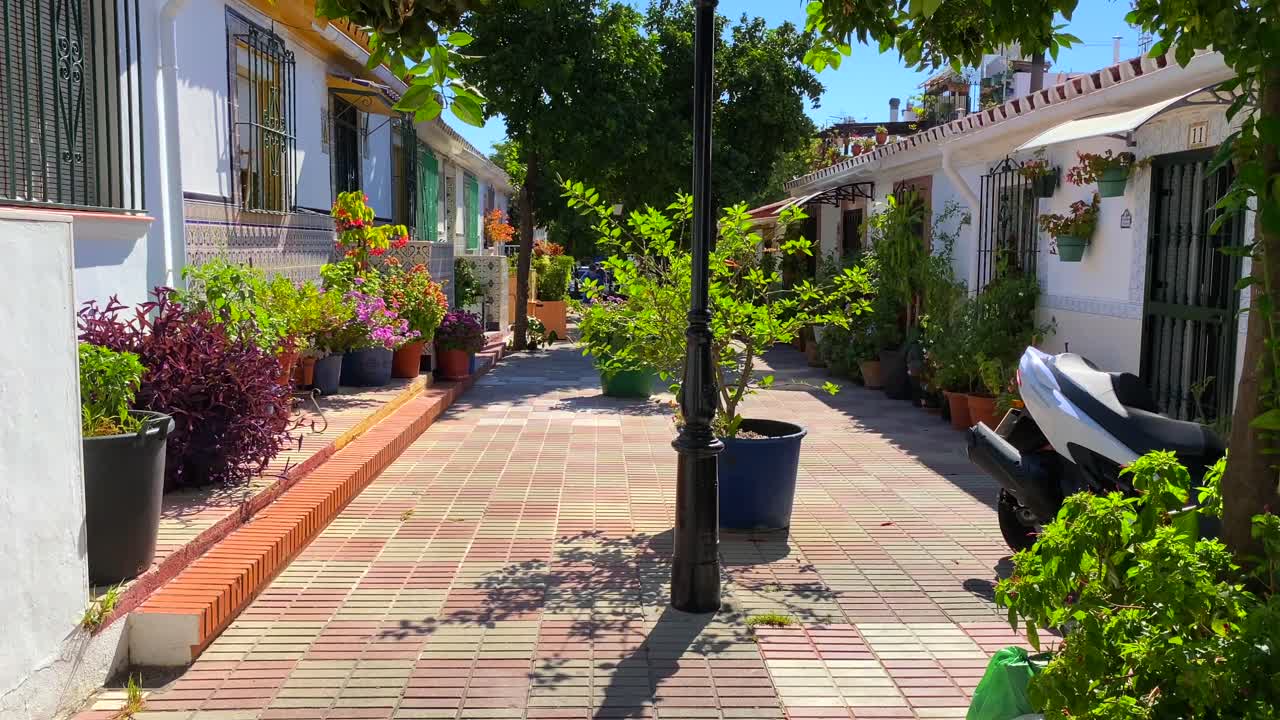 Aranci e bellissimi fiori in una tipica stradina spagnola stretta con case nel centro storico di Marbella, Spagna, giornata di sole e cielo blu, 4K con inclinazione verso l'alto