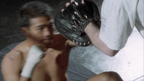 a boxer practices punching with the help of another person wearing a glove