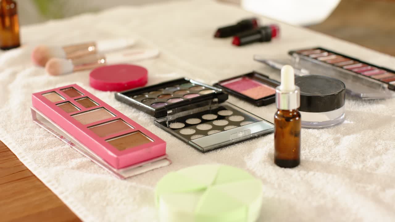 Die Kamera fährt auf ein weißes Handtuch zurück und präsentiert eine Auswahl an Make-up und Hautpflegeprodukten auf einem Holztisch
