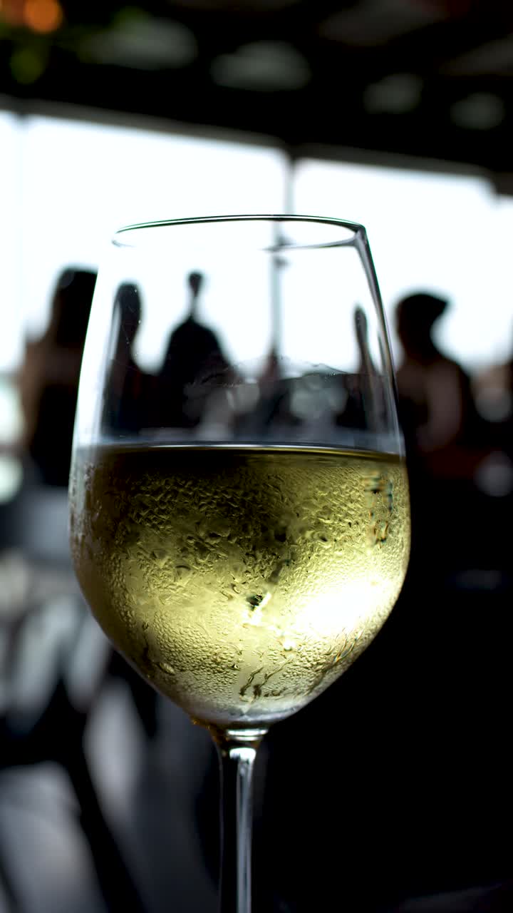 Primo piano di un bicchiere di vino bianco freddo con condensa su un patio di un ristorante all'aperto.