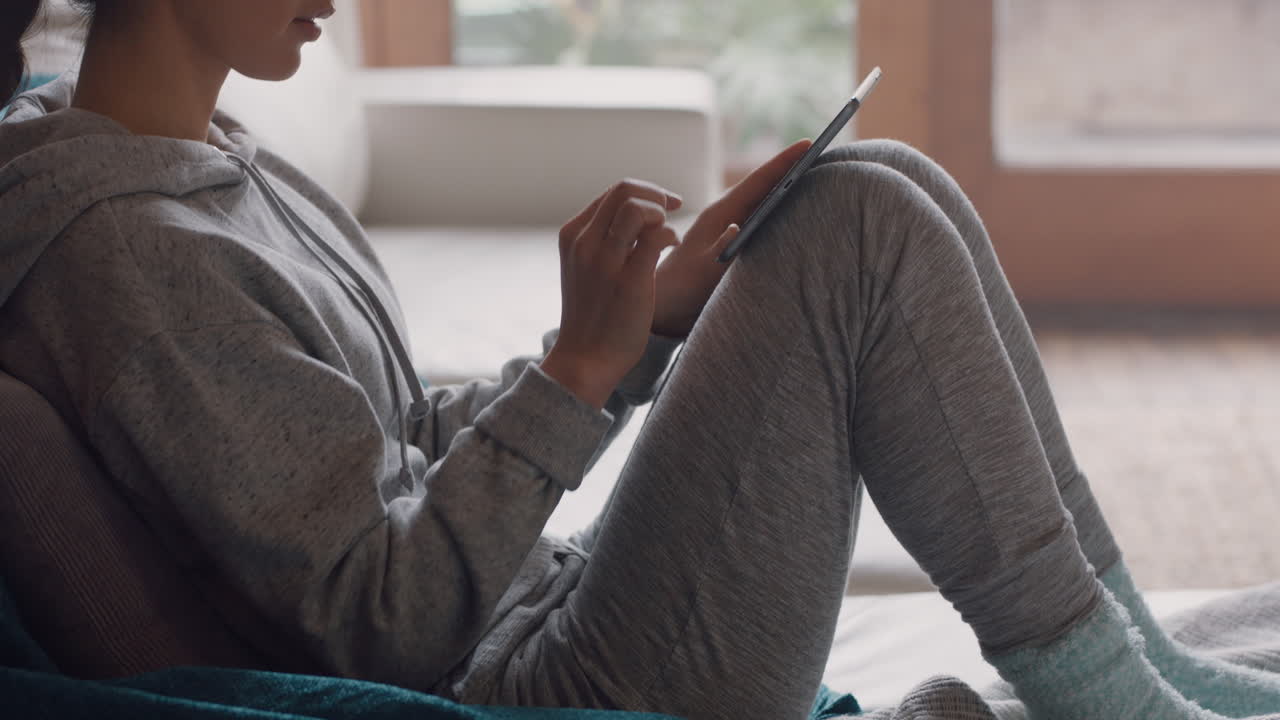 young woman using digital tablet at home browsing online reading social media messages enjoying relaxing lifestyle