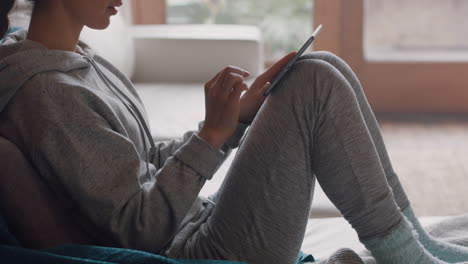 mujer joven usando una tableta digital en casa navegando en línea leyendo mensajes de redes sociales disfrutando de un estilo de vida relajado