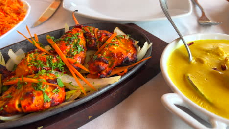 Traditionelles-Indisches-Chicken-Korma-Mit-Kokosreis-Und-Tandoori-Chicken-Tikka-Mit-Zwiebeln-Auf-Einer-Sehr-Heißen-Platte-Mit-Dampfrauch-In-Einem-Restaurant,-4k-Aufnahme