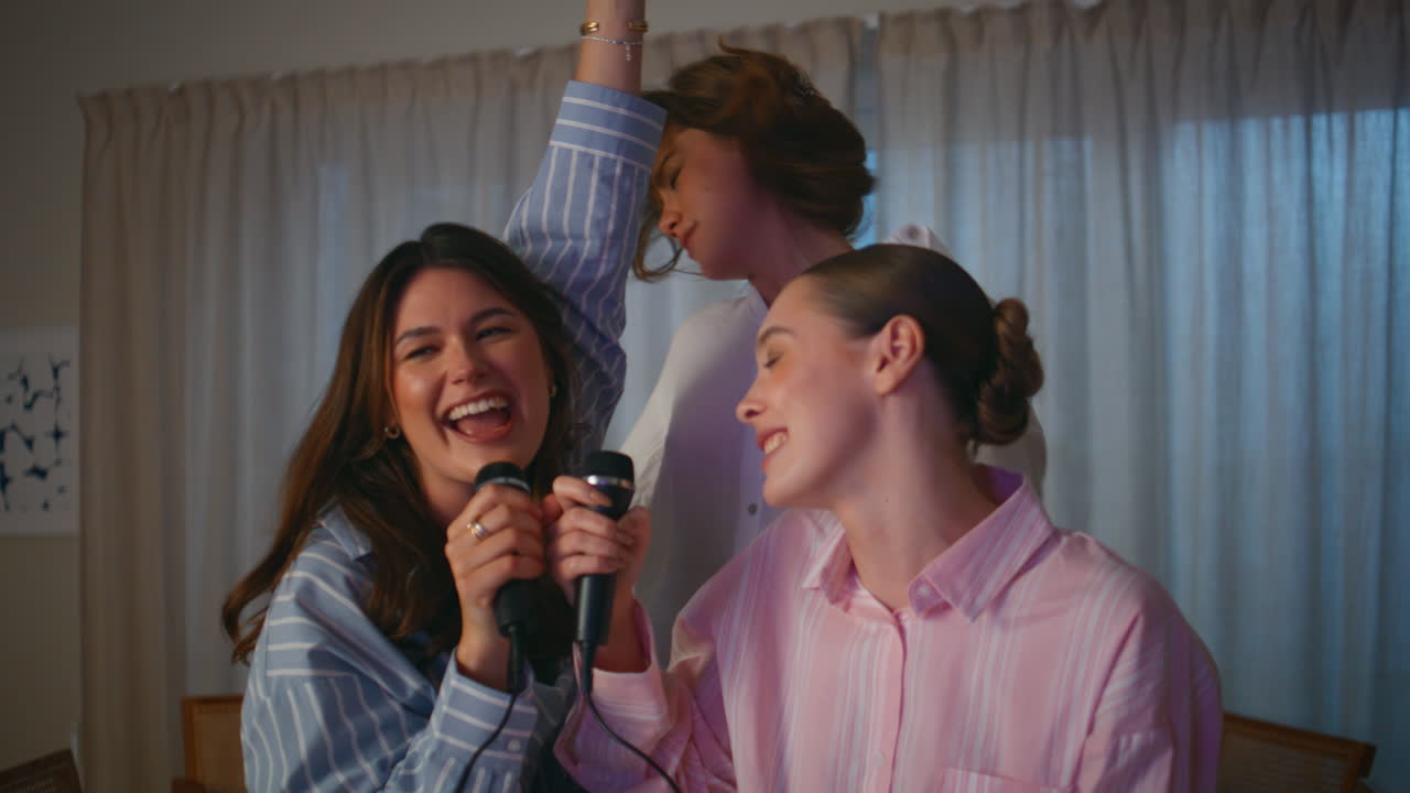 Girls singing microphone home pajamas party closeup. Emotional women karaoke