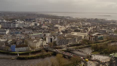 Un-Dron-Asciende-Por-Encima-De-Los-Observadores-Del-Desfile-Cruzando-Un-Extraño-Puente-Salmón-Sobre-El-Río-Corrib-En-Galway,-Irlanda