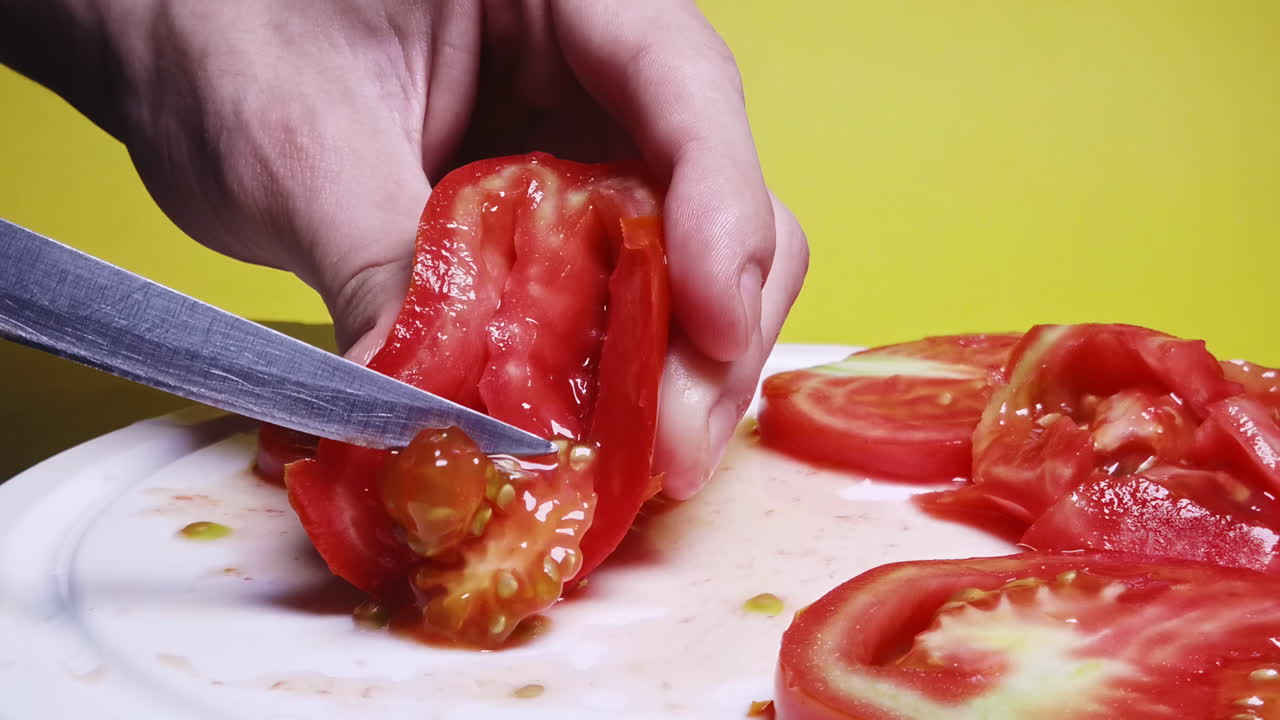 Close-up shot of a man cutting tomato on the desk in slowmotion in front of a yellow background