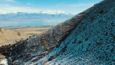 ladera nevada con vistas a un valle, un lago y montañas cubiertas de nieve a lo lejos - vista aérea deslizante