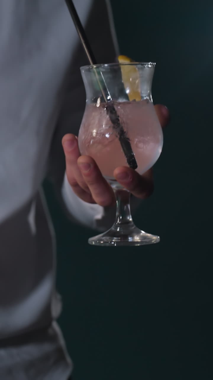 Primo piano di un uomo che indossa una camicia bianca e pantaloni grigi, che tiene in mano una stecca da biliardo e un bicchiere di limonata con una cannuccia nera. Cubetti di ghiaccio e una fetta di limone galleggiano nel bicchiere mentre lo solleva per bere un sorso.