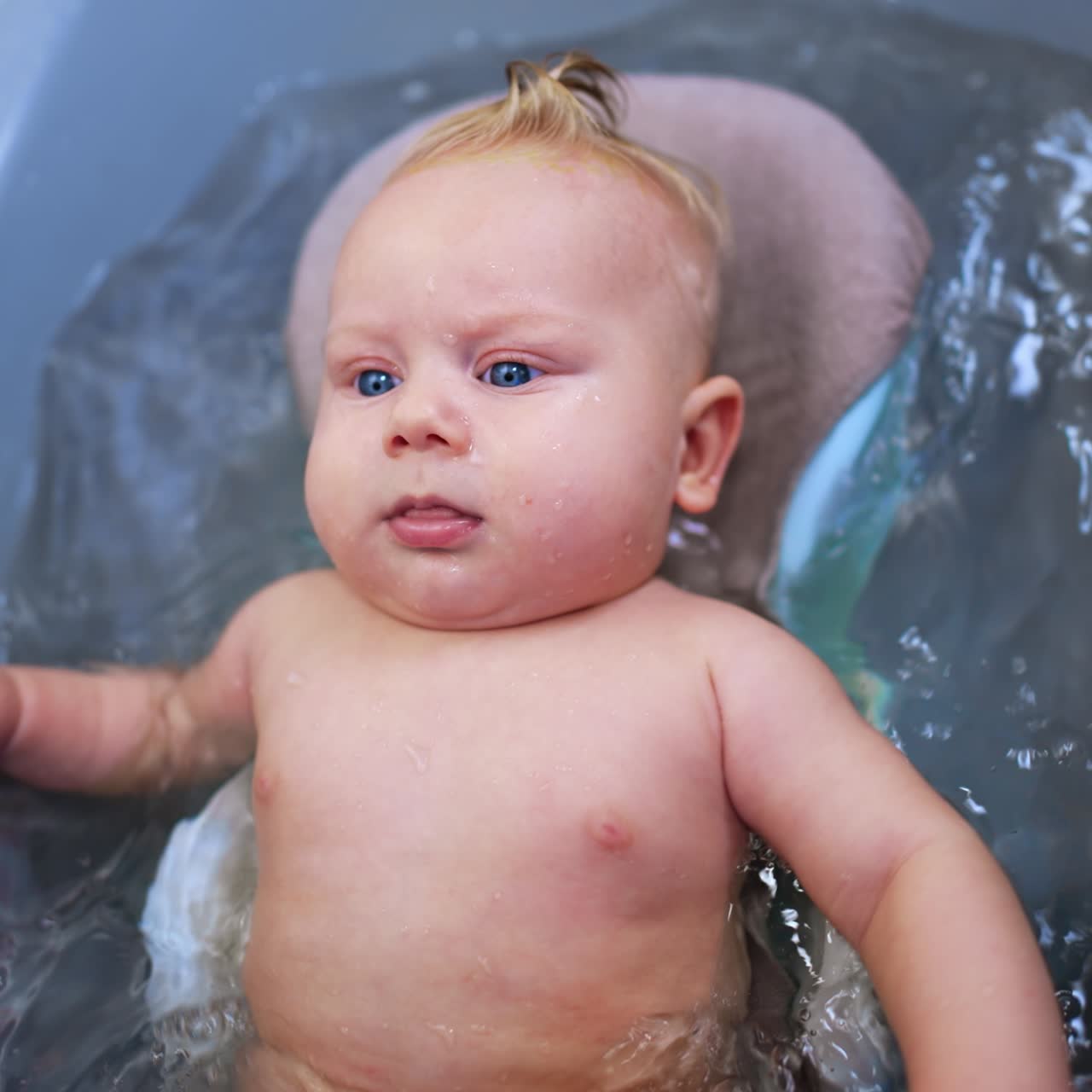 Bebê adorável relaxado no banho. Criança fofa e rechonchuda acenando ativamente com as mãos e os pés na água