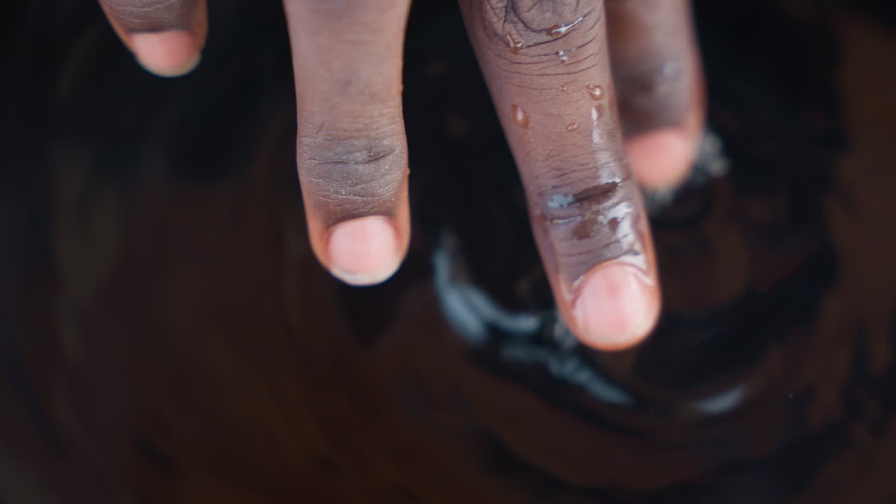 Black carpenter fingers dipped in stain, closeup of dusty fingertips pressing into glossy finish, sawdust flecks and gentle ripples, tactile inspection and focus on grain and coating in workshop