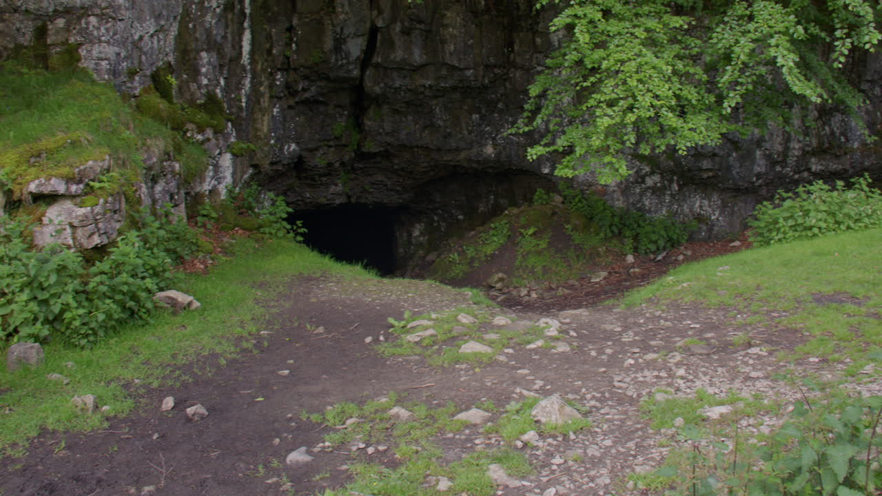 Plano panorâmico amplo subindo até as árvores na caverna de Yordas, mostrando a entrada para a caverna de calcário e as cachoeiras