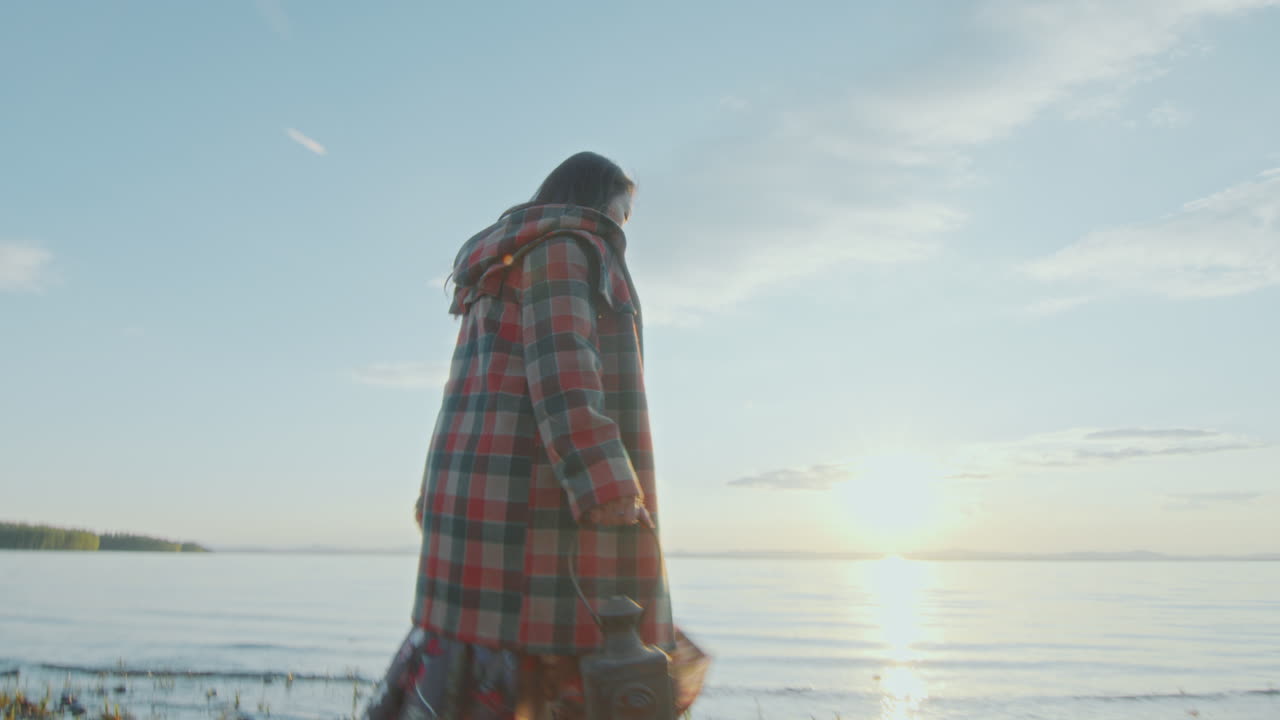 해가 지면 호수 연안 의 연못 을 가로질러 걸어가는 등불 을 들고 있는 젊은 여자