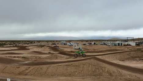 motorcycles jump dirt ramps on a racecourse on an overcast day in slow motion aerial view