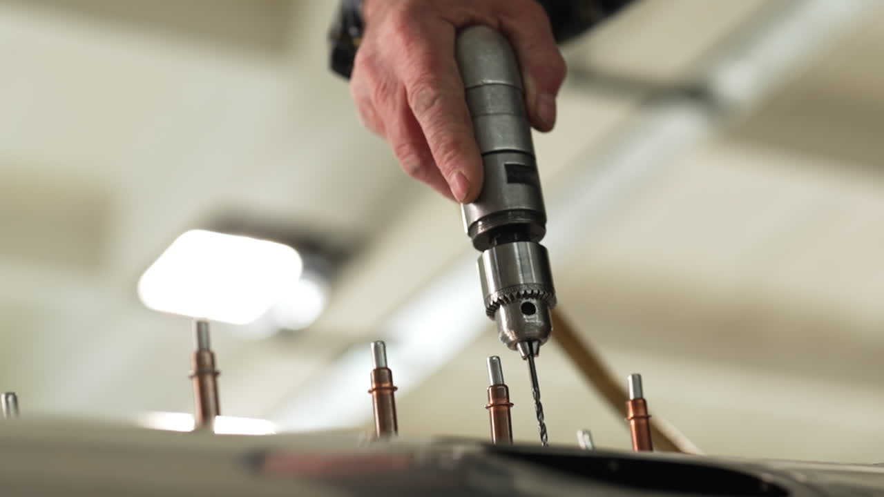 Worker using a drill press to secure rivets on a sheet metal panel in an industrial manufacturing process