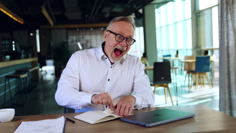 irritated man sitting at desk pulls the page out of his notebook. man grimacing much and puts the piece of paper to his mouth.