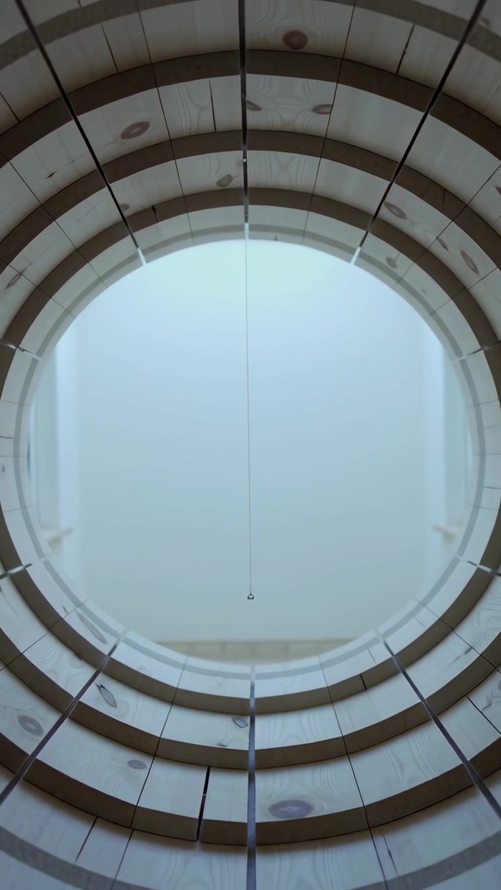 Vertical video: Pulling back camera revealing concentric wooden rings in atrium with hanging cord