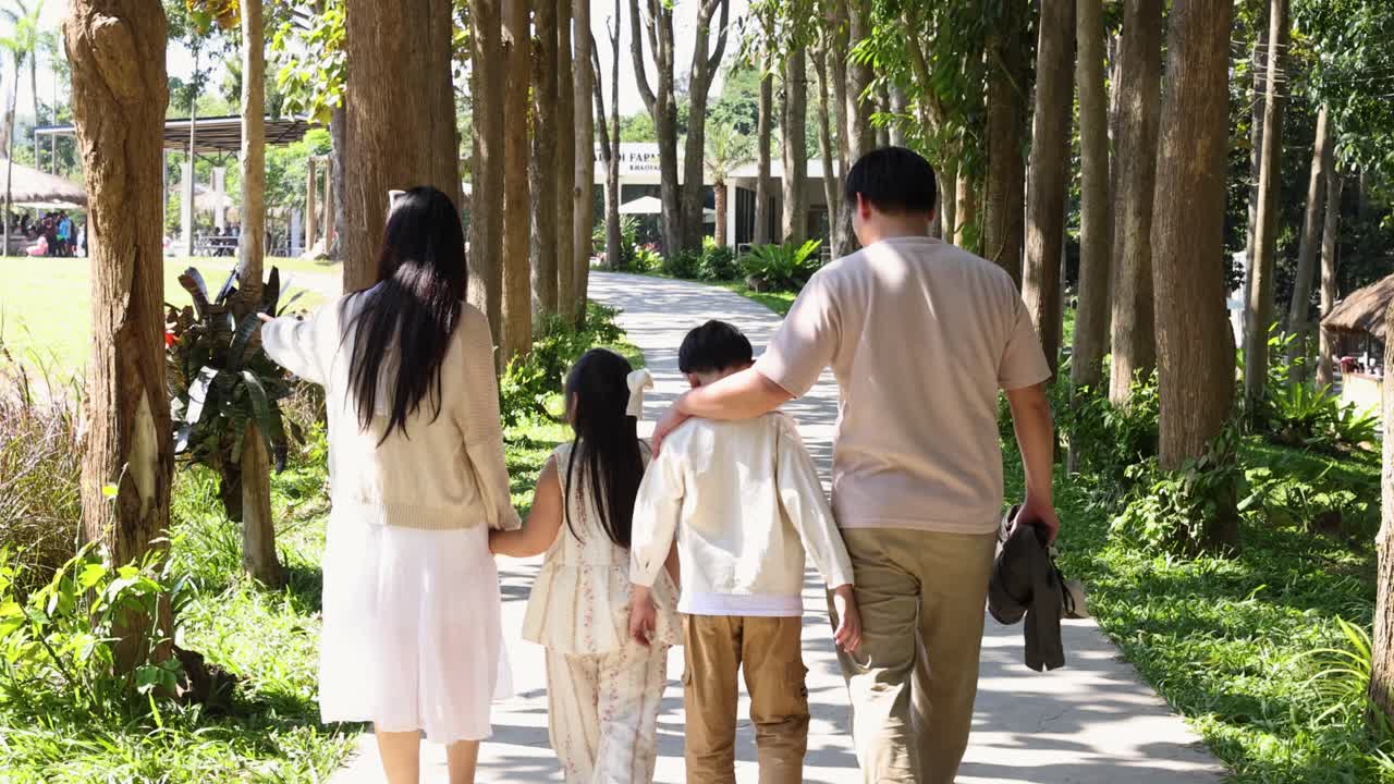 明るい自然光の中、並木道の公園の小道を散策する家族の後ろ姿。
