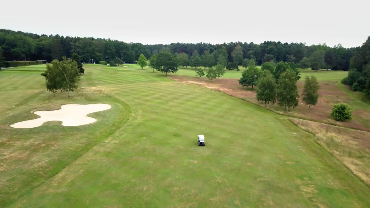 Aerial view of a golfer driving golf cart car on a golf course between forest trees