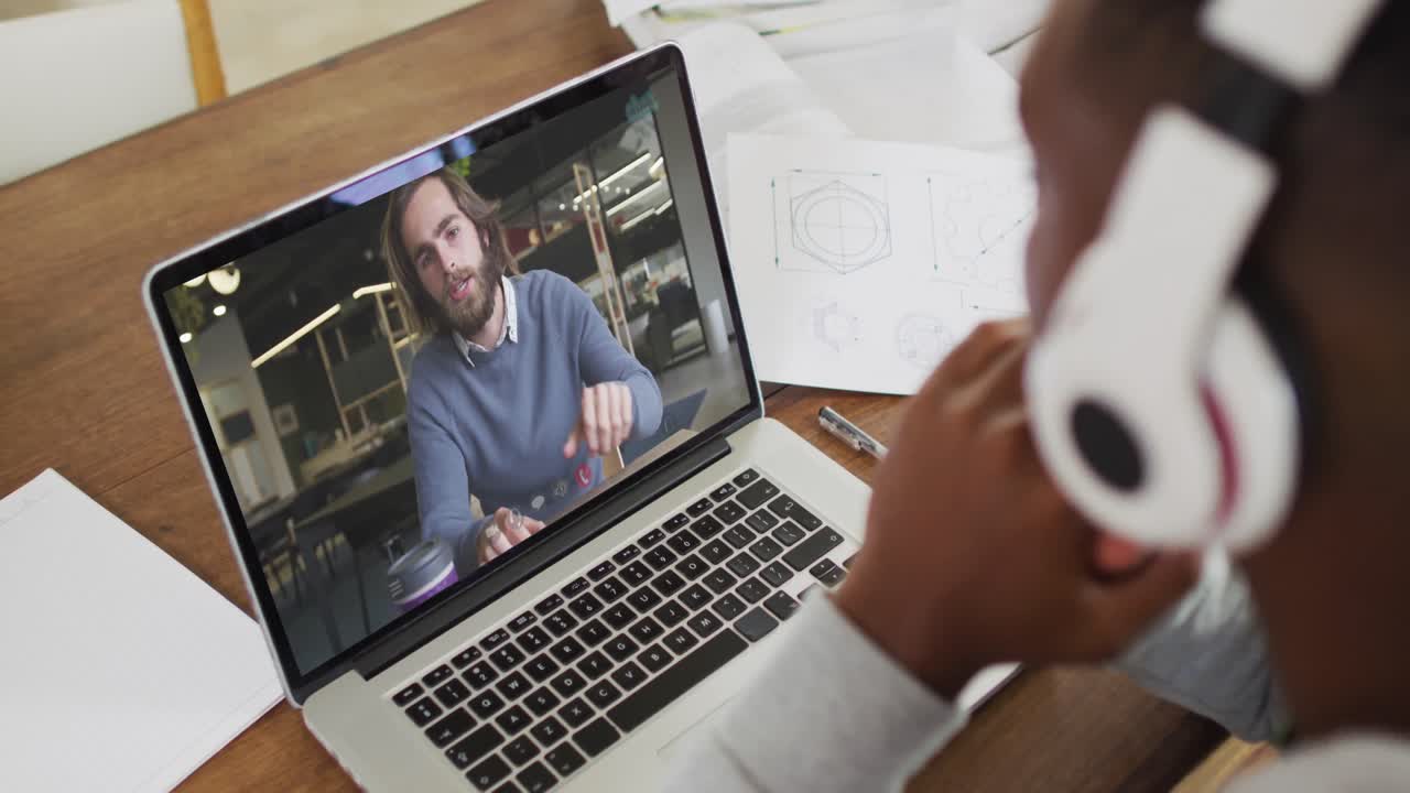 African american male college student holding notes while having a video call on laptop at home