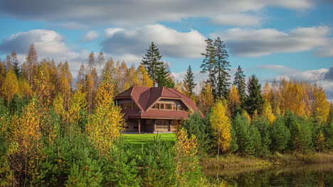 Timelapse-shot-of-warm-autumn-day-in-rural-countryside-with-view-of-a-beautiful-wooden-two-storied-cottage-by-the-side-of-a-lake